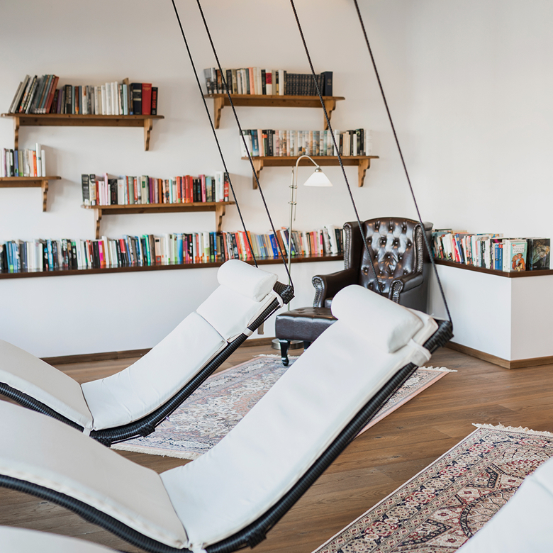 Gemütlicher Leseraum mit hängenden weißen Liegen, Ledersessel und wandmontierten Bücherregalen.