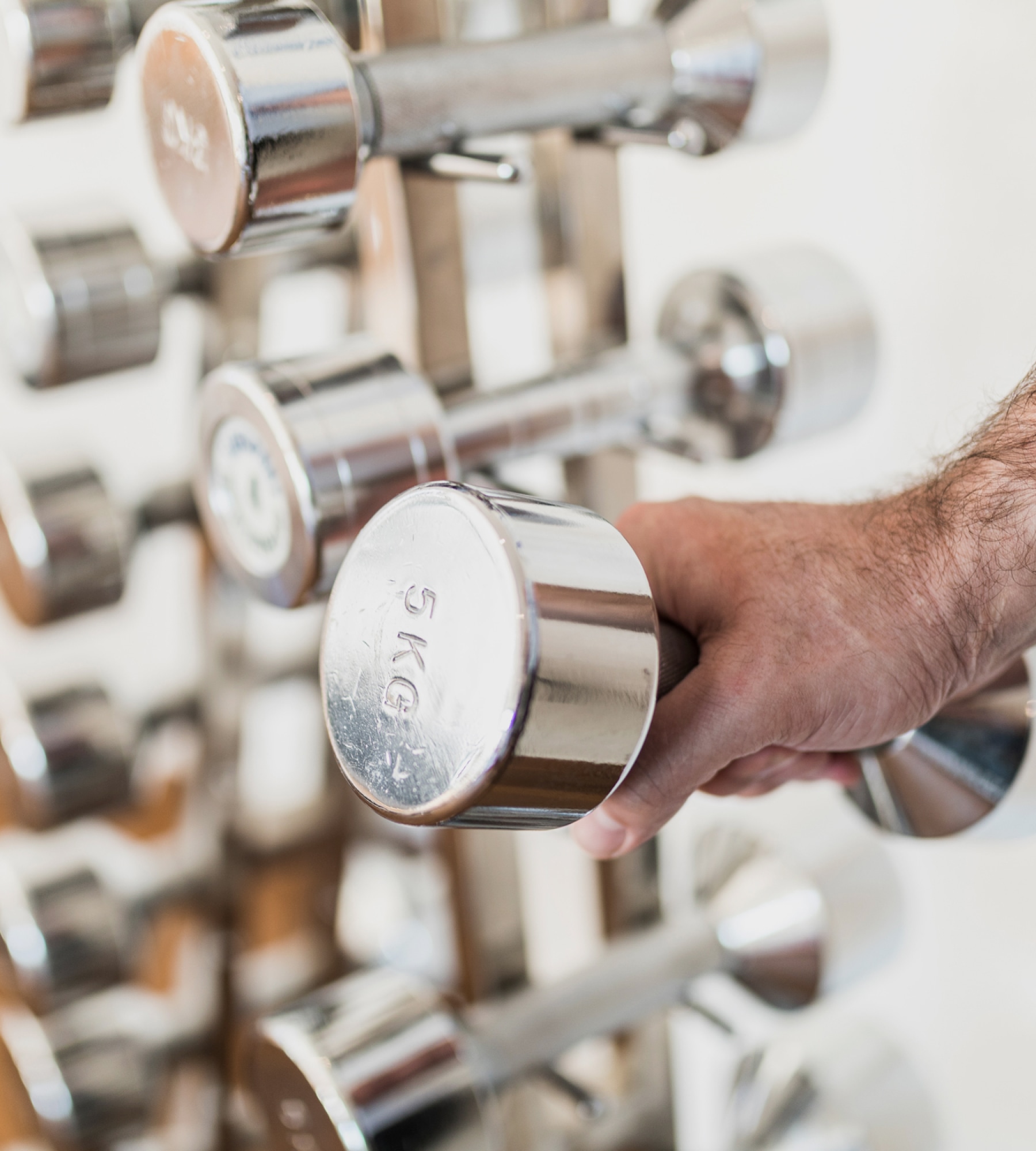 Eine Hand greift nach einer glänzenden 5-kg-Chromhantel aus einem Hantelständer im Fitnessstudio.