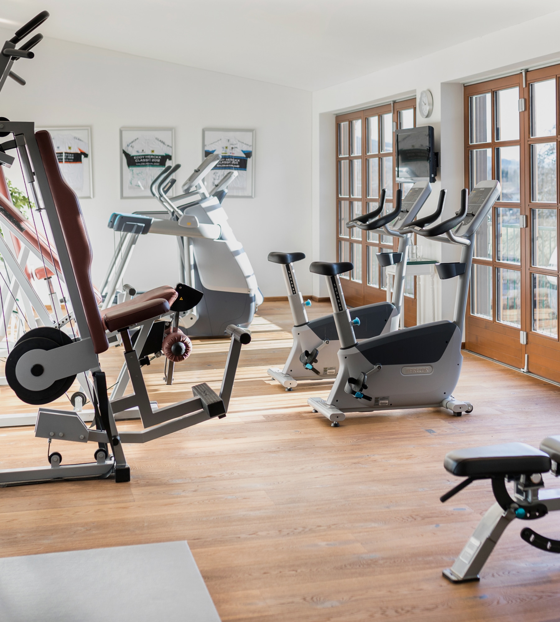 Heller Fitnessraum mit Holzboden, Ergometern, Kraftgeräten und großen Glastüren im Hotel Post Lermoos.